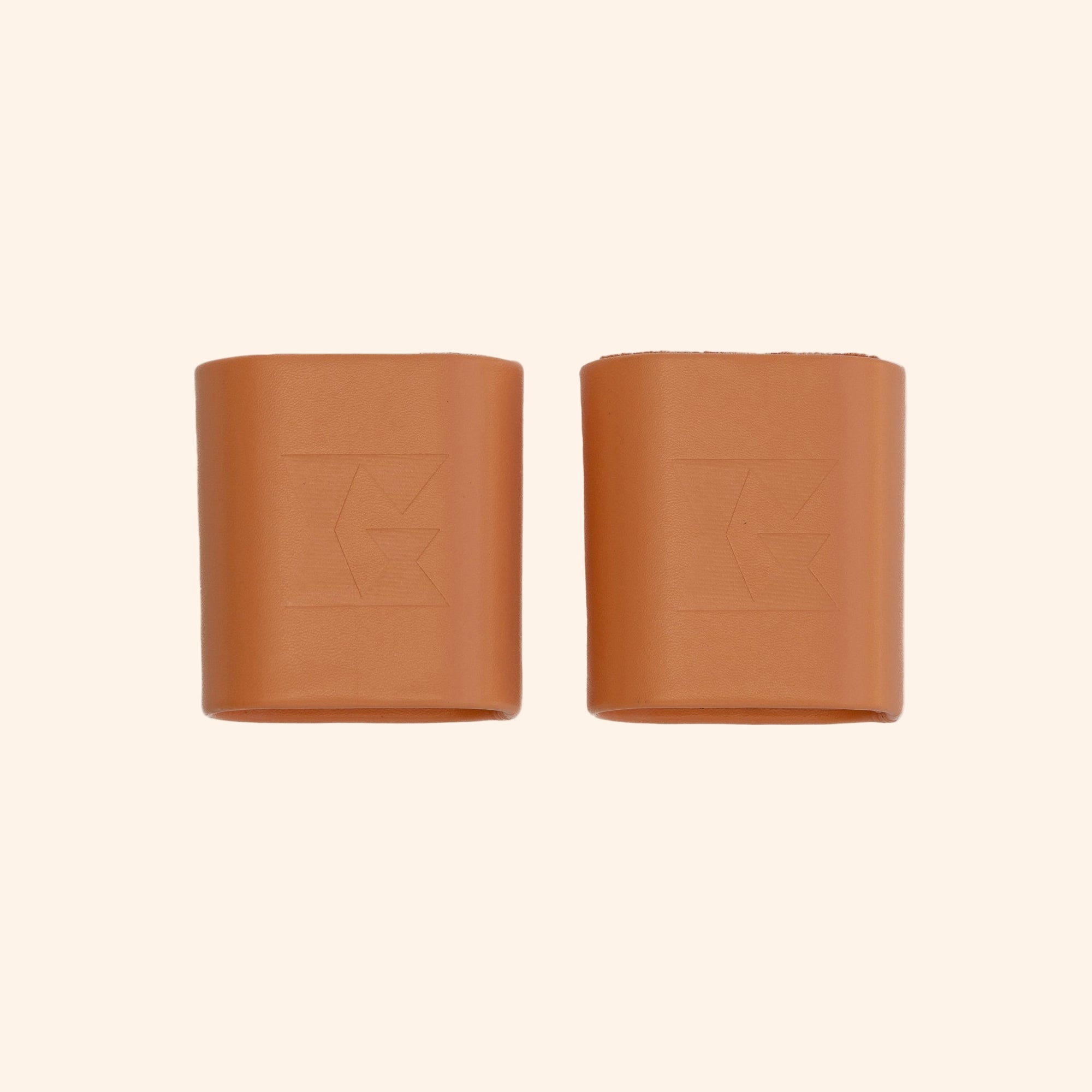 Pair of tan leather dice cups with Gammn logo embossed on each, side by side on white background